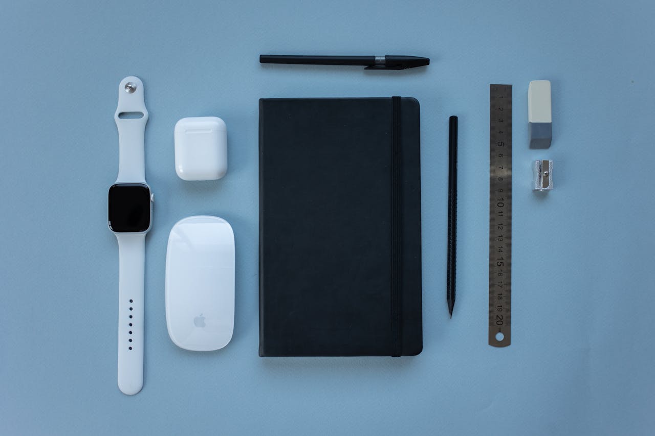 Modern tech gadgets and stationery arranged on a soft blue background in a flat lay style.